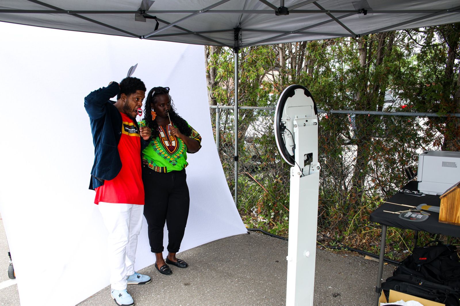 Two guests posing with props in front of a white backdrop, facing the photo booth